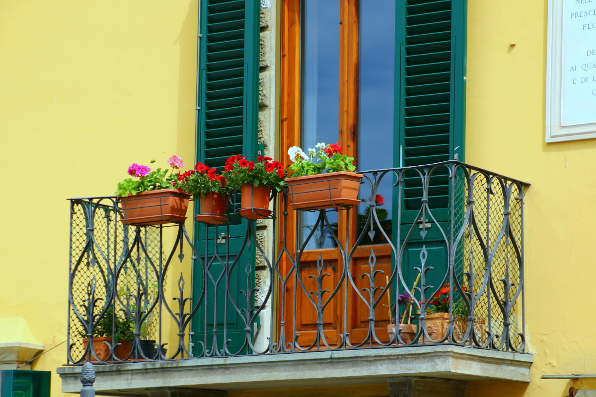 Balcone con vasi di fiori colorati e persiane verdi su facciata gialla.