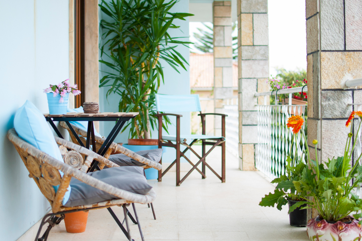 Balcone arredato con tavolino, sedie e piante in vaso, ambiente luminoso e accogliente.