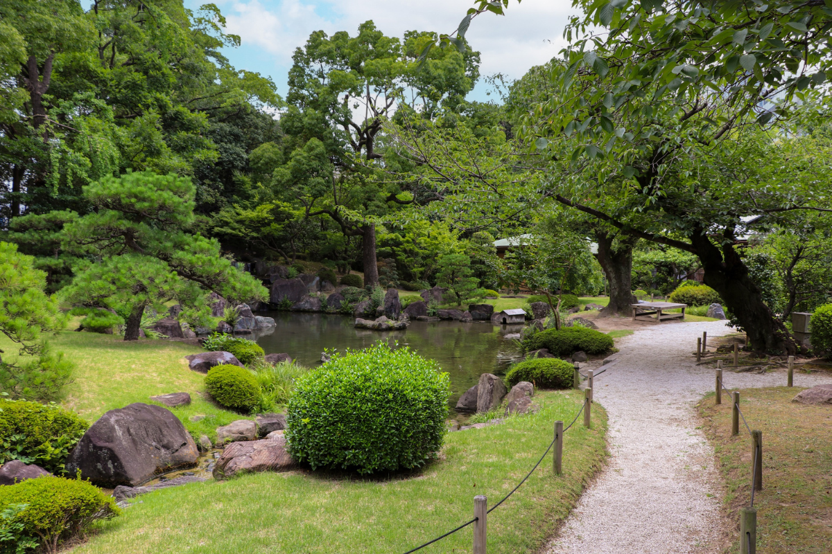 Paesaggio di giardino giapponese con acqua, rocce e percorso in ghiaia.