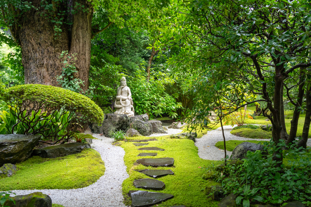Giardino giapponese con percorso in pietra tra muschio e alberi.