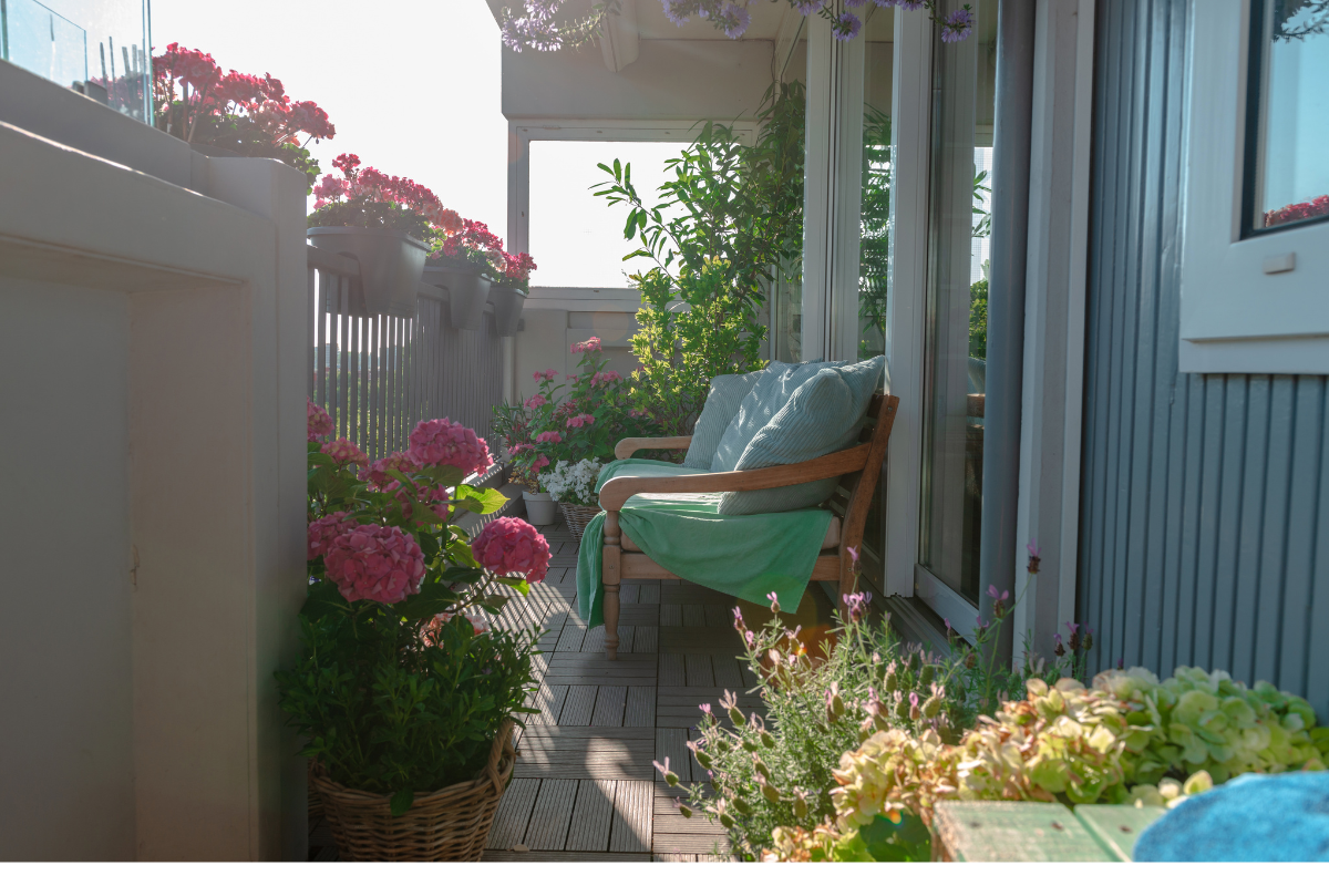 Balcone stretto con sedia, piante e fiori in vaso illuminati dalla luce del sole.