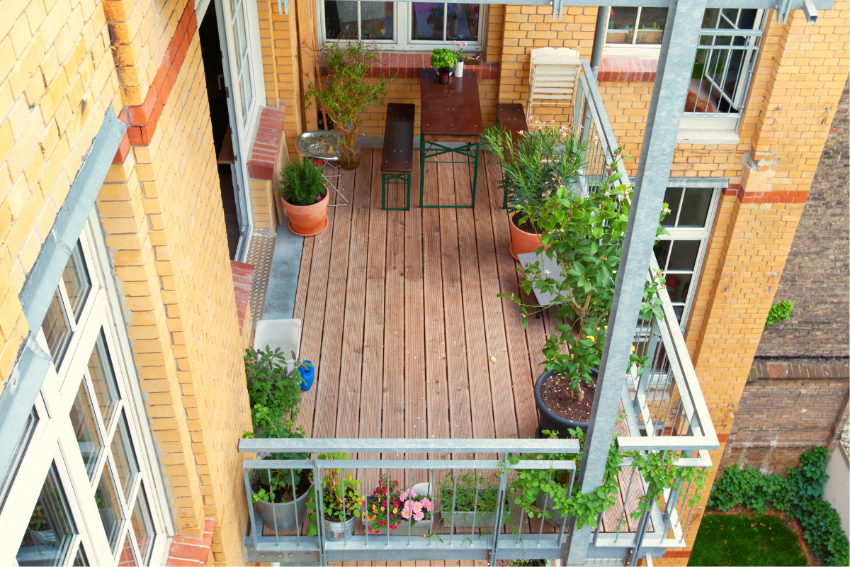 Terrazzo in legno con tavolo, sedie e piante in vaso, visto dall’alto in ambiente urbano.