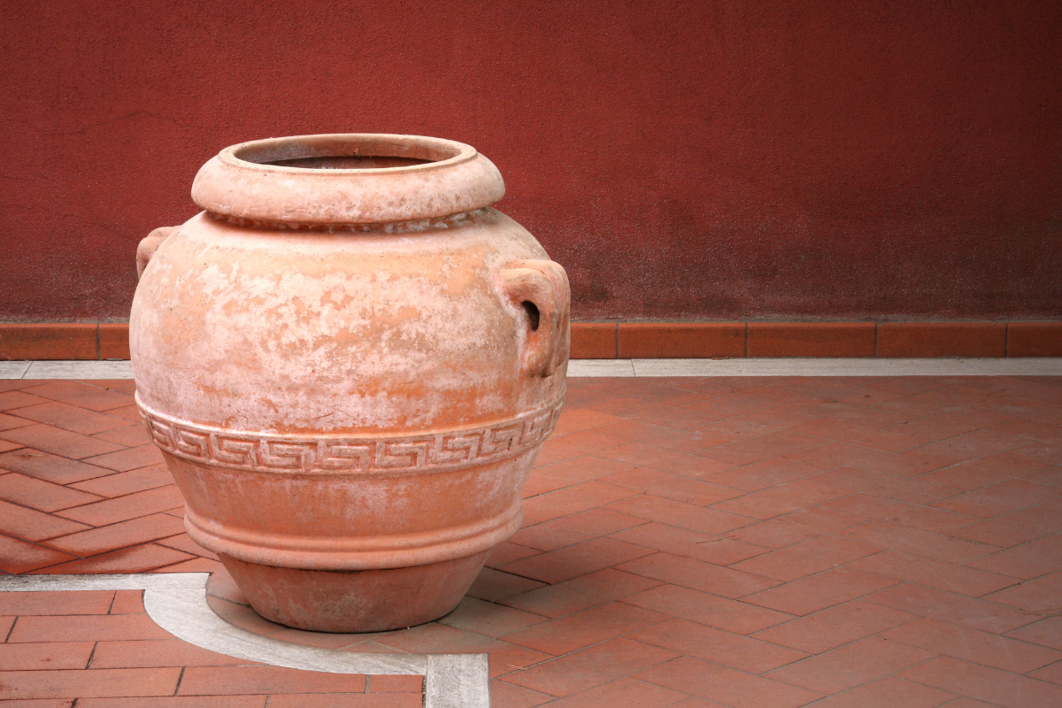 Grande vaso in terracotta decorato, posizionato su pavimento in cotto davanti a parete rossa.