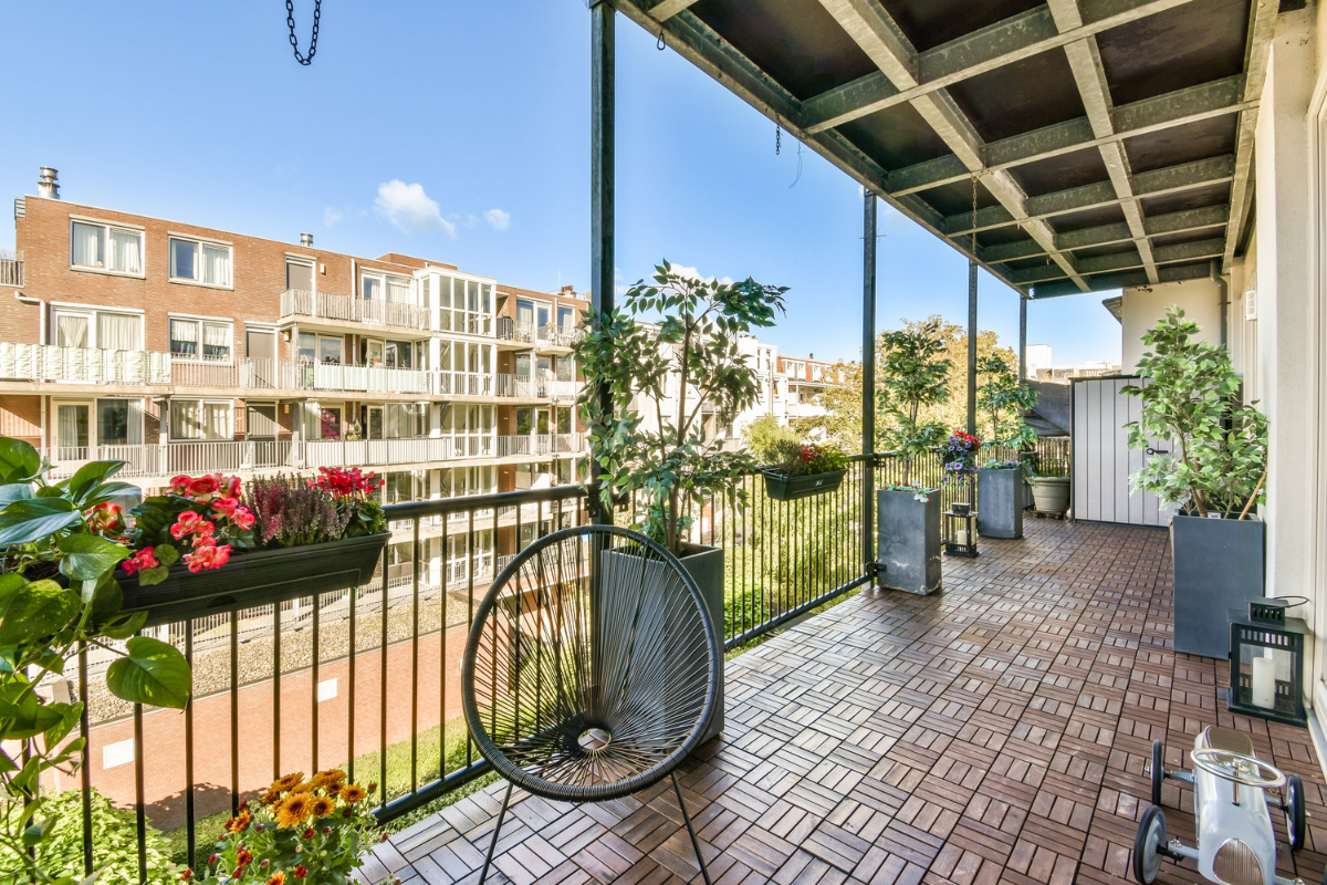 Balcone lungo con pavimento in legno, piante in vaso, bicicletta e vista su quartiere residenziale.