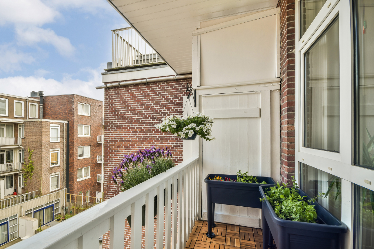 Balcone urbano con fioriere e piante in vaso, vista su edifici residenziali.