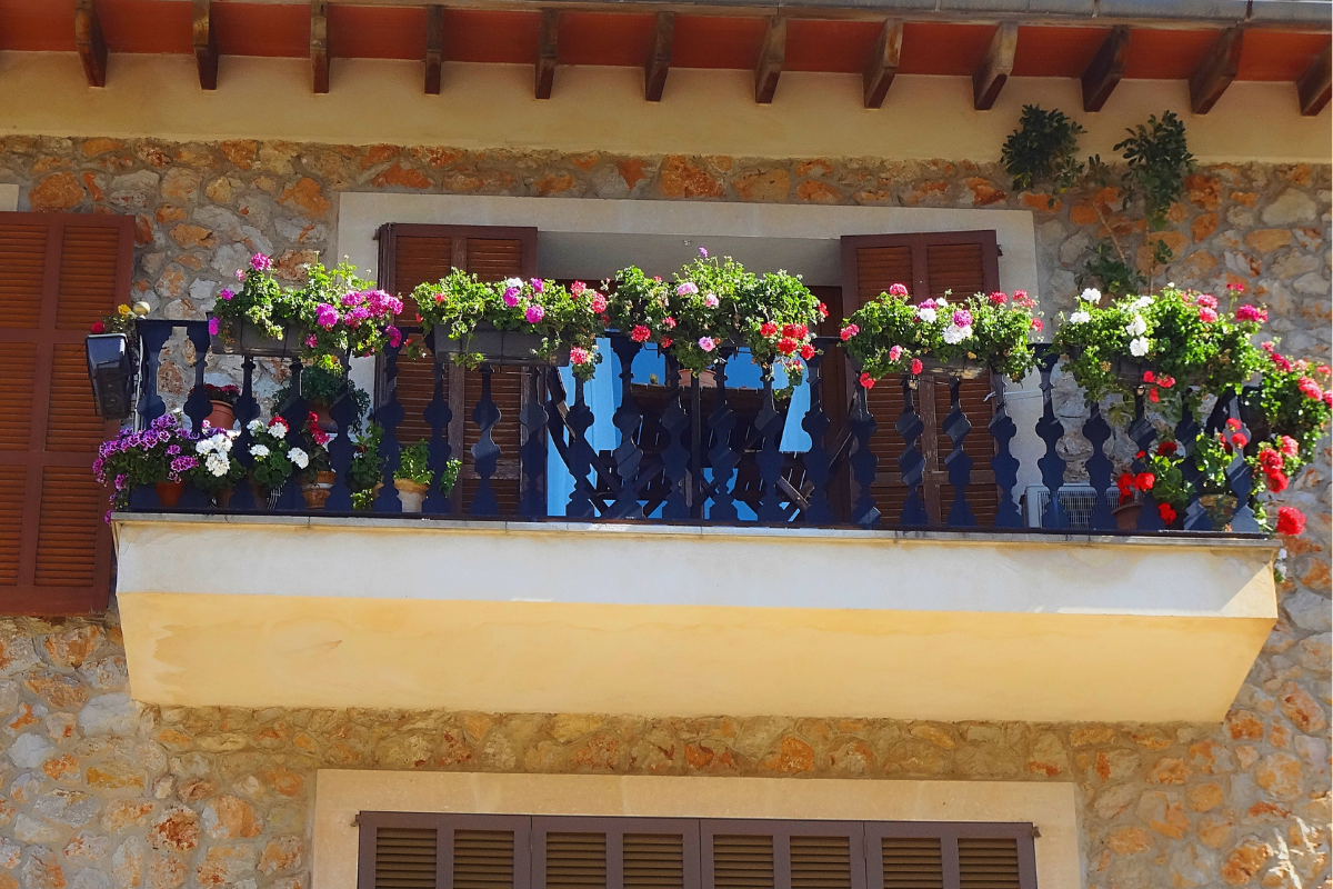 Balcone in pietra con fioriere ricche di fiori colorati su ringhiera in legno.